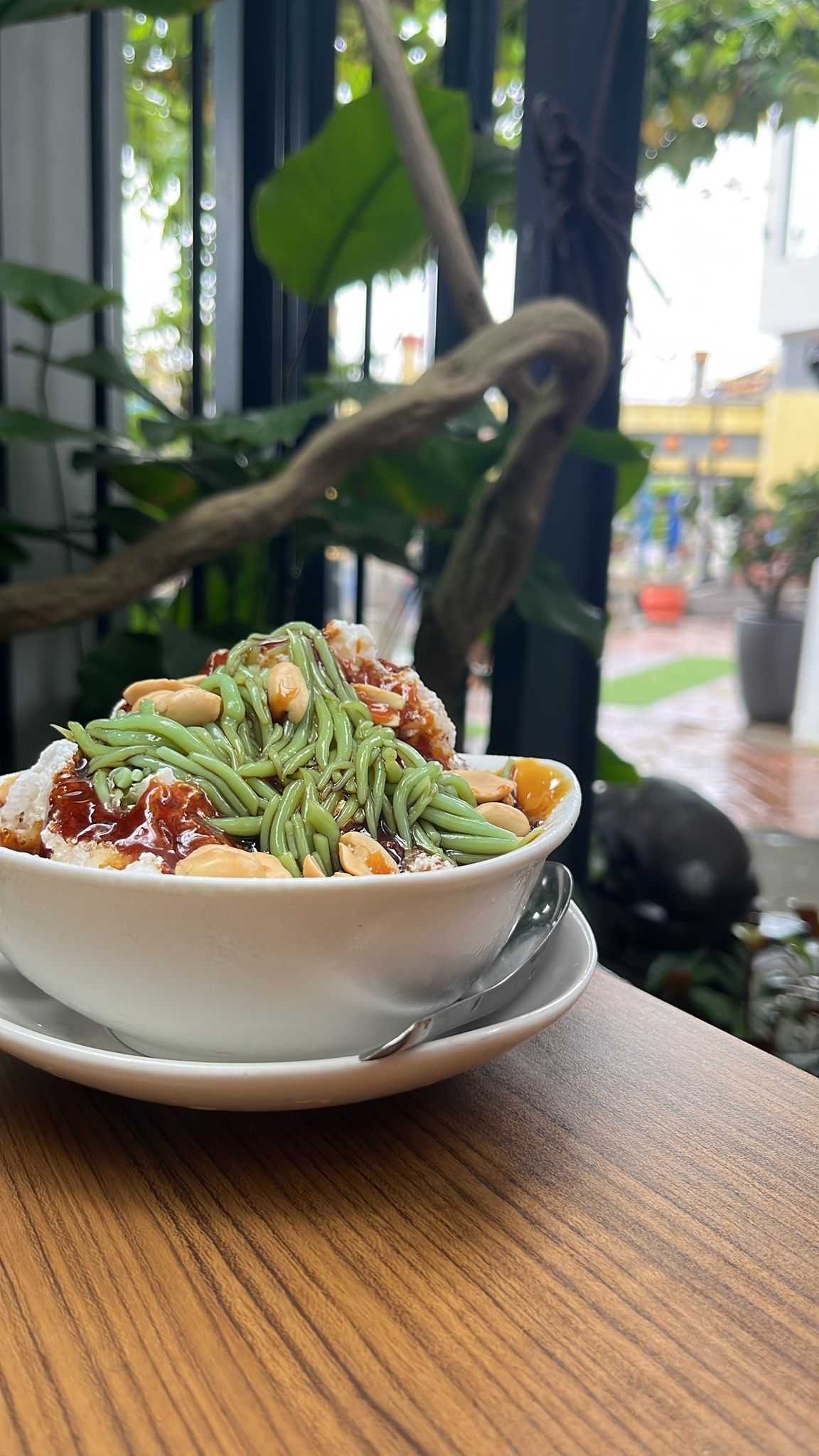 A bowl of cendol with green strands, syrup and peanuts